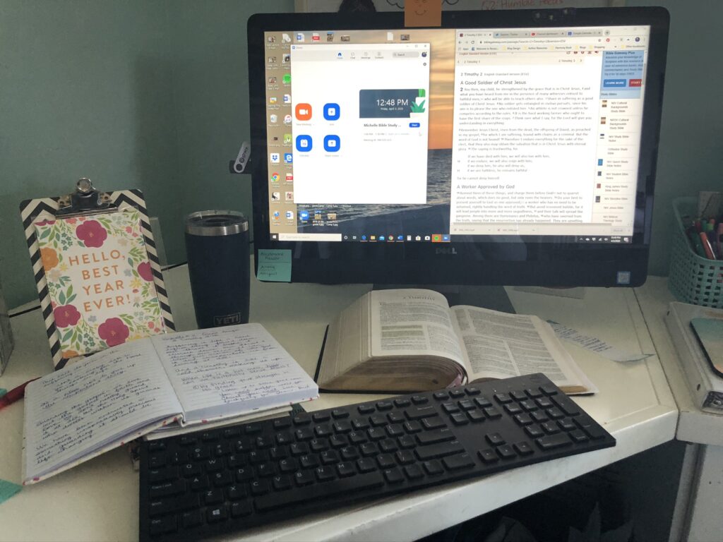 An open Bible, notebook, and a coffee cup sit in front of a computer with Zoom open on the screen.
