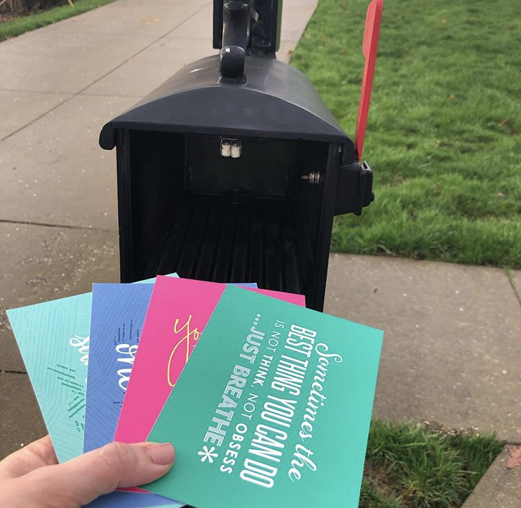 The author's hand holds four brightly colored postcards, pointed into an open mailbox.
