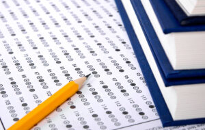 A sharp pencil rests on top of a bubbled-in Scantron type of score sheet. Two blue books are stacked on the right edge of the image.