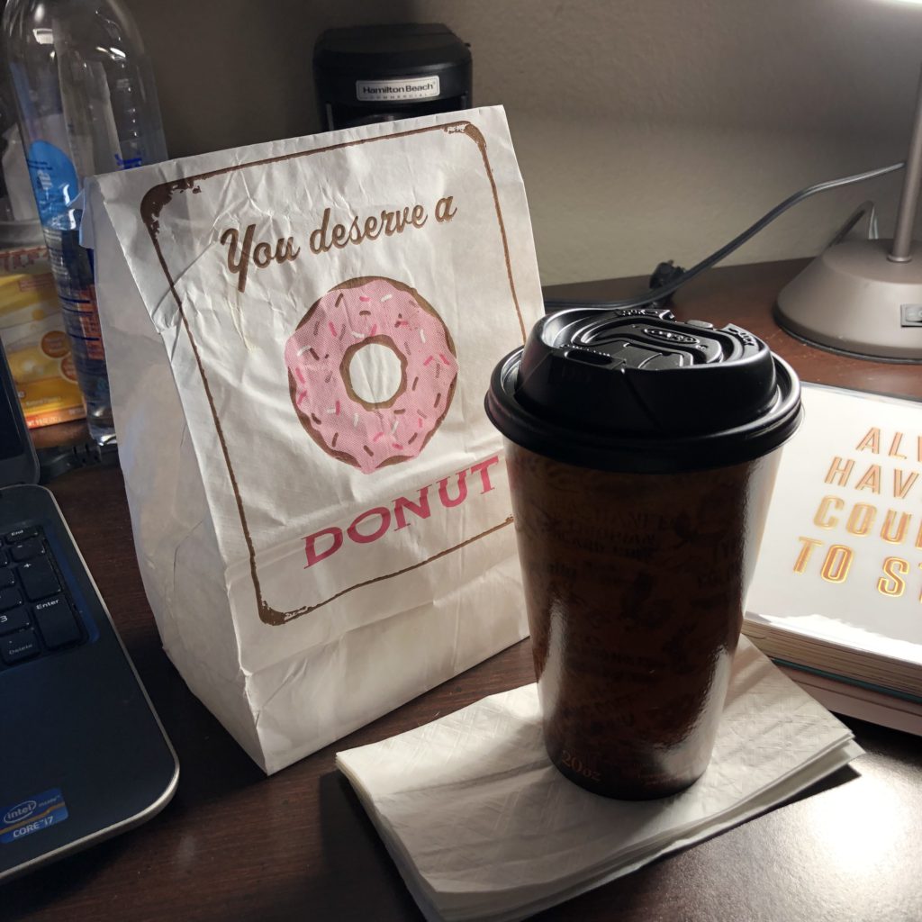 Bag of donuts and cup of coffee beside an Erin Condren Life Planner.