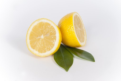 A fresh lemon arranged in two halves against a pair of green leaves.