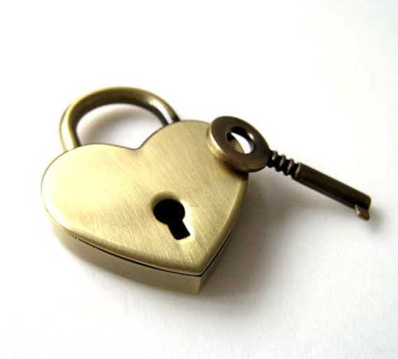 a brass heart-shaped lock lays beside a brass key